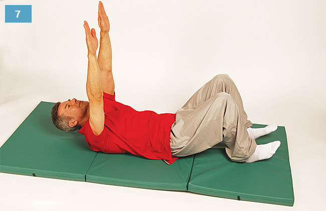 Ćwiczenie w leżeniu na plecach, głowa uniesiona, ręce wyprostowane nad głową, pięty oparte na materacu